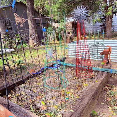 Sale Photo Thumbnail #93: Assorted metal garden decor, including wire trellises, decorative tomato cages, a red metal windmill obelisk, and a vintage-style cast iron hand pump decor piece.
