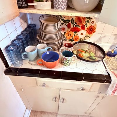 Sale Photo Thumbnail #66: Assorted kitchenware including blue drinking glasses, ceramic mugs, stackable stoneware dishes, and floral serving trays.