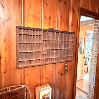 Sale Photo Thumbnail #74: Vintage wooden printer's tray mounted on wood-paneled wall, featuring numerous small compartments.