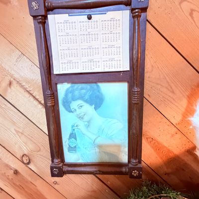 Sale Photo Thumbnail #104: Vintage Coca-Cola advertising calendar housed in a dark wooden frame with spindle side columns and decorative floral corner accents.