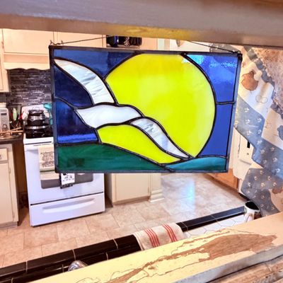 Sale Photo Thumbnail #72: Handcrafted stained glass window panel featuring a sun and wave design in bright blue, yellow, green, and white art glass.