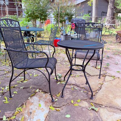 Sale Photo Thumbnail #86: Black wrought iron outdoor bistro set featuring a round mesh table and matching armchairs with leaf-motif backrests.
