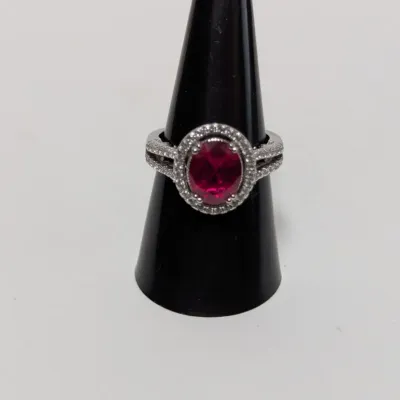Sale Photo Thumbnail #949: Silver-tone ring featuring a large oval red center stone surrounded by a crystal halo setting with split-shank details.