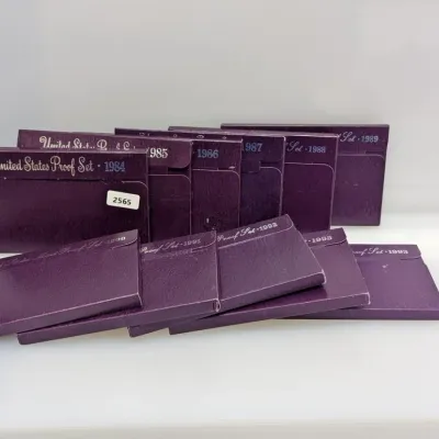 Sale Photo Thumbnail #1060: A collection of United States Proof Sets in purple original government packaging, spanning dates from 1984 through 1993.
