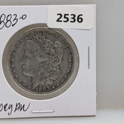 Sale Photo Thumbnail #1027: 1883-O Morgan silver dollar mounted in a cardboard coin flip holder labeled with handwritten text and a lot sticker.
