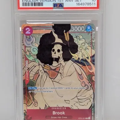 Sale Photo Thumbnail #68: PSA 10 Gem Mint graded 2024 One Piece English 1st Anniversary Set Brook card (#011). Encased in a protective clear slab.