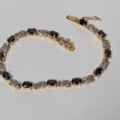 Sale Photo Thumbnail #973: Gold-tone tennis bracelet featuring oval black gemstones alternating with diamond-accented X-links and a secure box clasp with safety latch.