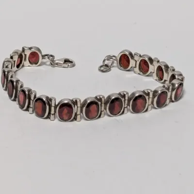 Sale Photo Thumbnail #970: Sterling silver line bracelet featuring bezel-set oval garnet gemstones with a lobster claw clasp.