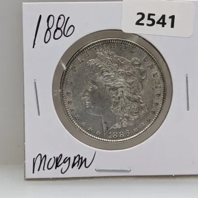 Sale Photo Thumbnail #1032: 1886 Morgan silver dollar coin housed in a protective cardboard flip.