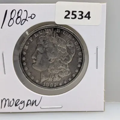 Sale Photo Thumbnail #1025: 1882-O Morgan silver dollar displayed in a cardboard coin flip, featuring dark toning and visible surface wear.