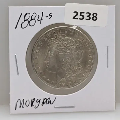 Sale Photo Thumbnail #1029: 1884-S Morgan silver dollar coin housed in a cardboard 2x2 coin holder flip.