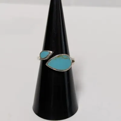 Sale Photo Thumbnail #958: Southwestern-style sterling silver ring featuring two teardrop-shaped inlaid turquoise stones, displayed on a ring cone.