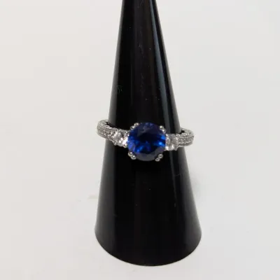 Sale Photo Thumbnail #951: Sterling silver ring featuring a round-cut deep blue center stone flanked by clear cubic zirconia accents and micro-pave detailing.