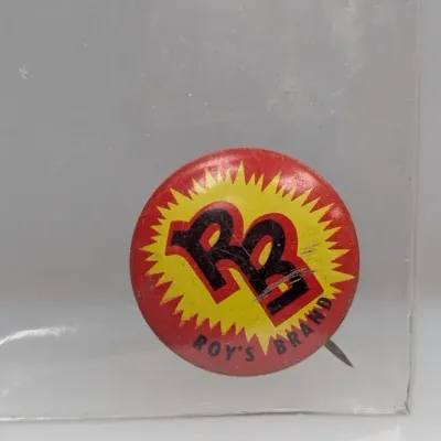 Sale Photo Thumbnail #117: Vintage Roy's Brand RB lithographed pinback button, featuring red, yellow, and black graphics with light surface scratches.