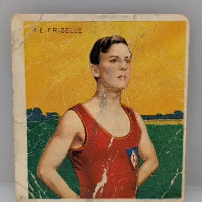 Sale Photo Thumbnail #293: Vintage Ogden's cigarette card featuring R.E. Frizelle in athletic wear against a yellow and green background. The card shows heavy wear with noticeable creasing, surface cracking, and edge abrasion.