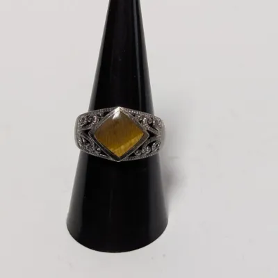 Sale Photo Thumbnail #955: Vintage sterling silver ring featuring a diamond-shaped tiger's eye gemstone and intricate filigree scrollwork detail, displayed on a ring cone.