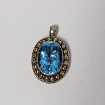 Sale Photo Thumbnail #978: Oval faceted blue topaz pendant set in a sterling silver bezel with gold-tone beaded accents.