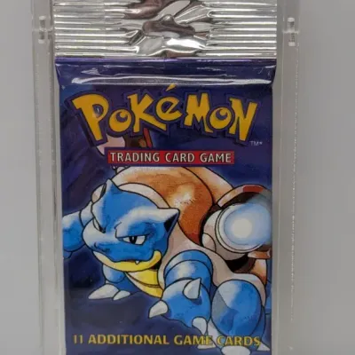 Sale Photo Thumbnail #26: Sealed 1999 Pokémon Base Set booster pack featuring Blastoise artwork, preserved inside a hard plastic protective case.
