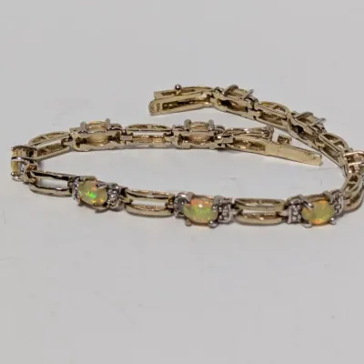 Sale Photo Thumbnail #974: Gold tennis bracelet featuring oval-cut opal cabochons flanked by small accent stones with a box clasp.