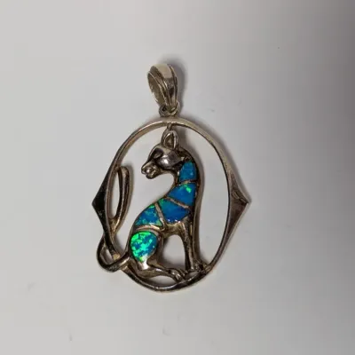 Sale Photo Thumbnail #985: Sterling silver seated cat pendant featuring blue and green inlaid opal panels within an openwork oval frame.
