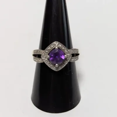 Sale Photo Thumbnail #948: Vintage sterling silver ring featuring a central round purple amethyst stone surrounded by a textured, diamond-shaped halo setting with pavé accents along the band.