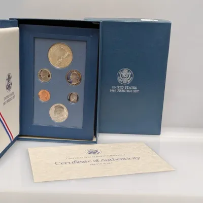 Sale Photo Thumbnail #1055: United States 1987 Prestige Set containing proof coins and a commemorative Constitution dollar, complete with original presentation case and Certificate of Authenticity.