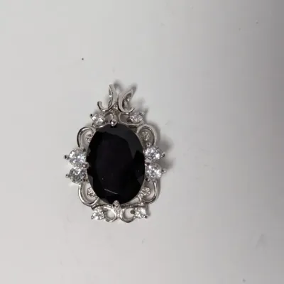 Sale Photo Thumbnail #989: Silver-tone pendant featuring an oval faceted black gemstone encircled by a halo of clear rhinestone accents in a filigree setting.
