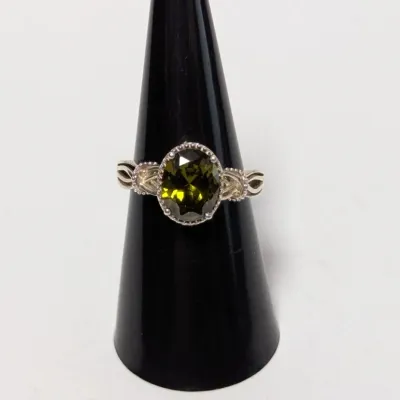 Sale Photo Thumbnail #963: Sterling silver ring featuring an oval facet-cut olive green gemstone in a beaded bezel setting with a decorative woven band.