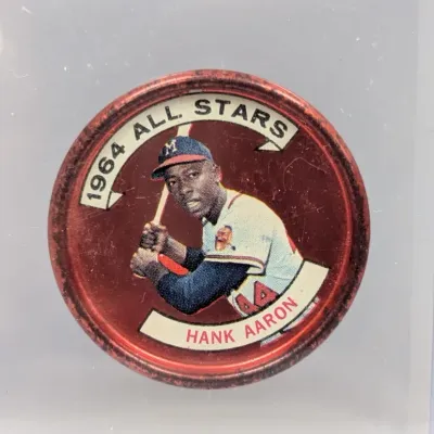 Sale Photo Thumbnail #128: Vintage 1964 Topps All-Stars Hank Aaron metal coin (#120), featuring the Milwaukee Braves hall-of-famer in a protective plastic holder.