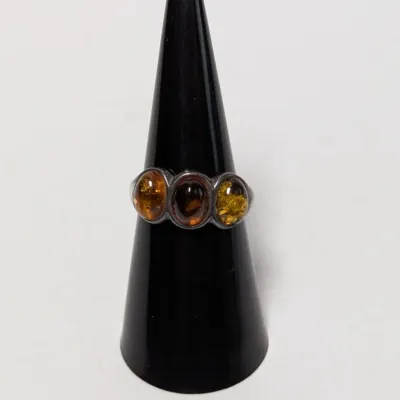Sale Photo Thumbnail #954: Silver ring featuring three bezel-set oval amber cabochons in varying honey and green tones, presented on a black ring display cone.