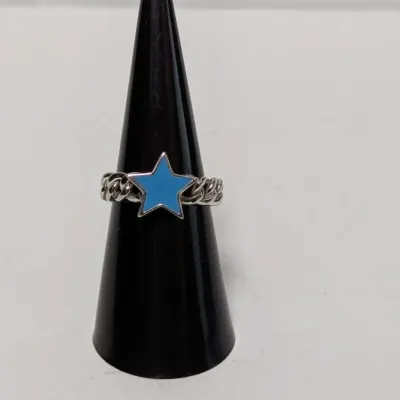 Sale Photo Thumbnail #962: Silver-tone chain-style ring featuring a light blue enamel star focal piece, displayed on a black ring cone.