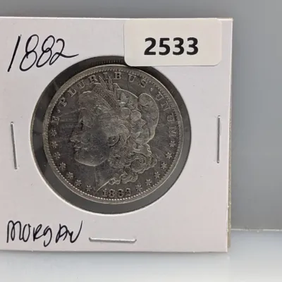 Sale Photo Thumbnail #1024: 1882 Morgan silver dollar coin housed in a protective cardboard flip binder holder.