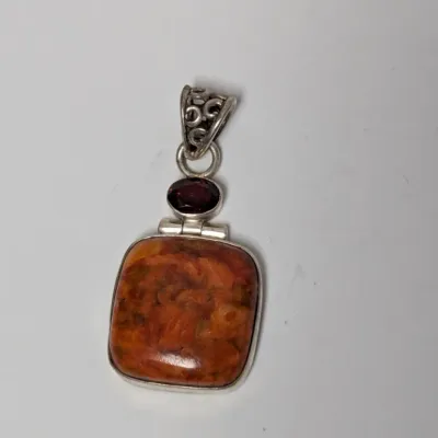 Sale Photo Thumbnail #979: Sterling silver artisan pendant featuring a large cushion-cut orange-brown spiny oyster or jasper stone accented with a small faceted dark red garnet and filigree bail.