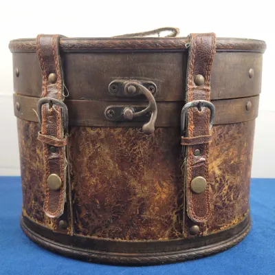 Vintage-style oval wooden storage box featuring leather trim, decorative brass hardware, and front buckle straps.