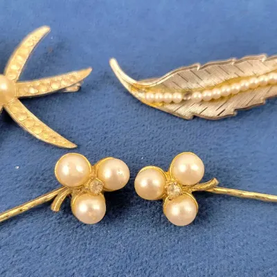 Collection of pearl-accented gold-tone hair accessories and brooches, including a starburst clip, textured feather pin, and a pair of...