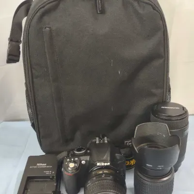 Nikon DSLR camera kit including body, attached lens, two additional lenses, battery chargers, and a black backpack case.