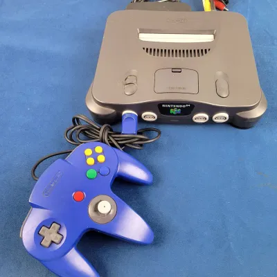 Nintendo 64 video game console system in charcoal grey, complete with power supply, AV cables, and a blue original controller.