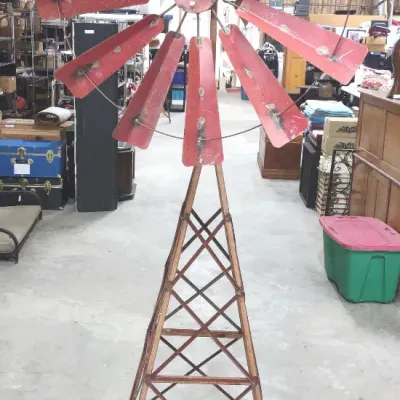 Vintage painted metal garden windmill with weathered red blades and a lattice metal tower stand.