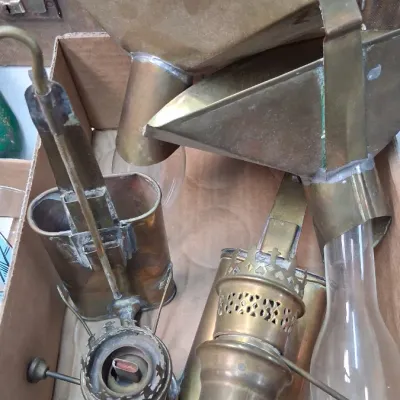 Collection of vintage brass oil lamp parts, including burners, shades, and glass chimneys, arranged in a cardboard box.