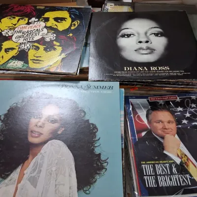 Collection of vintage vinyl LP records, including albums by Donna Summer, Diana Ross, and The Rascals, alongside printed memorabilia.