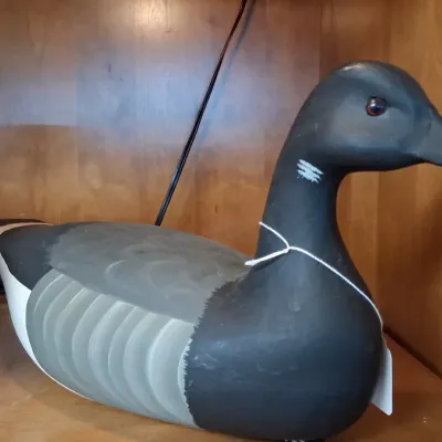 Hand-painted wooden goose decoy featuring gray, black, and white plumage detail with glass eyes, displayed alongside a red ceramic vase...