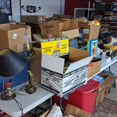 An assortment of estate sale goods including a display box of 1998 Pinnacle Inside sports trading card cans, table lamps, and various...