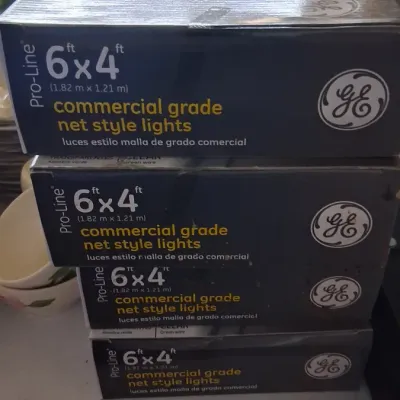 Stack of four boxed GE Pro-Line 6 ft x 4 ft commercial grade net style lights.