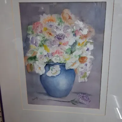 Framed watercolor painting depicting a bouquet of colorful pastel flowers in a blue vase, signed by the artist in the lower left corner.