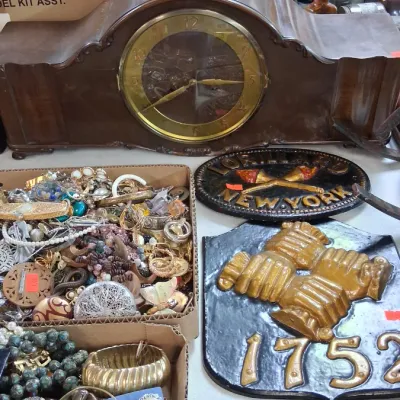 Vintage mantel clock with a dark wooden case, displayed alongside costume jewelry and cast iron decorative fire marks.
