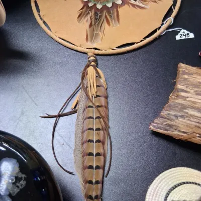 Native American-style framed leather wall art featuring a central feather star design and long hanging pheasant tail feathers.