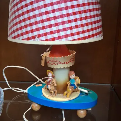 Vintage children's carousel table lamp with a red and white gingham shade, featuring miniature figures on a rotating base.