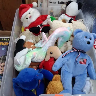 A clear plastic storage bin filled with vintage Ty Beanie Babies, including a blue USA bear, Santa Claus, and a iridescent dragon,...