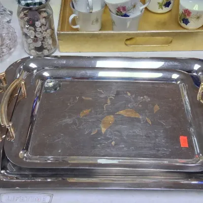 Pair of nested chrome serving trays with brass handles, featuring etched floral and leaf motifs on the tray surfaces.