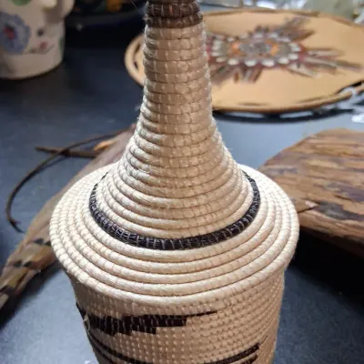 Hand-woven Rwandan Agaseke peace basket with a tall conical lid, featuring natural and dark brown geometric patterns.